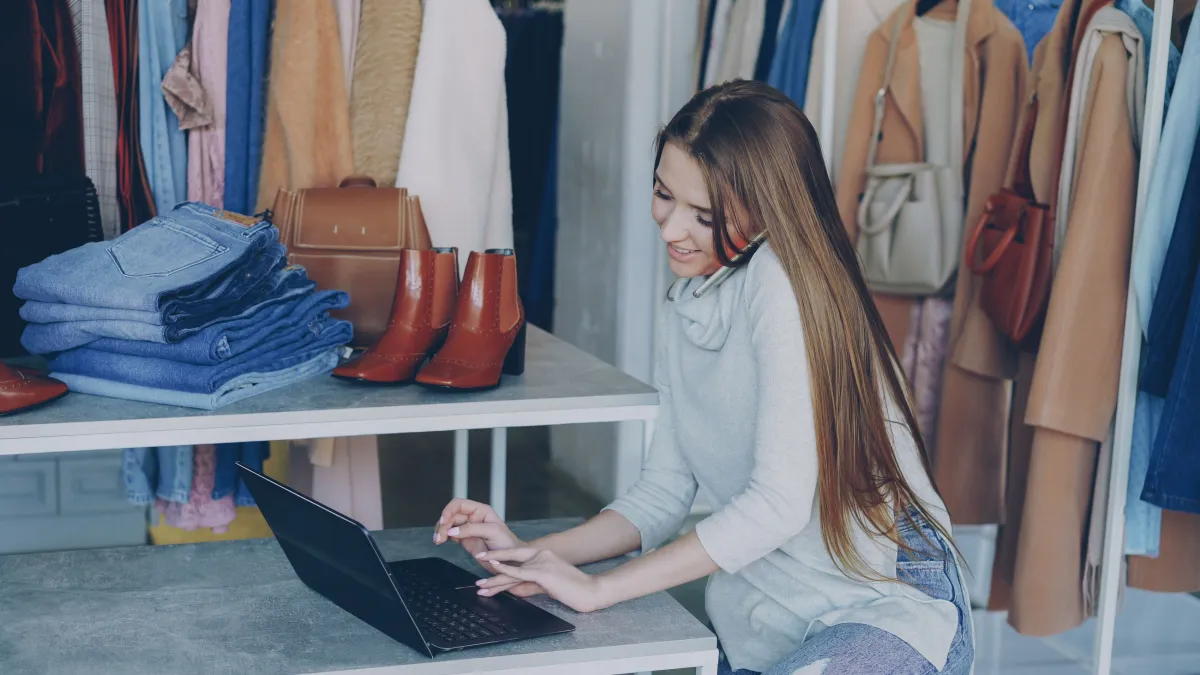 Comerciante utilizando notebook para administrar uma loja de roupas.