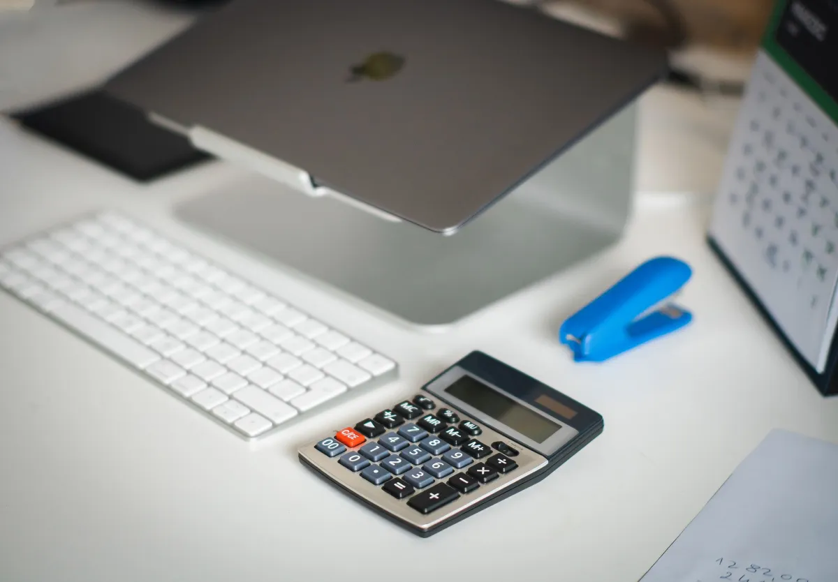 Calculadora financeira em uma mesa de escritório com notebook e caderno, usada para fazer contas e cálculos de orçamento ou despesas durante o trabalho