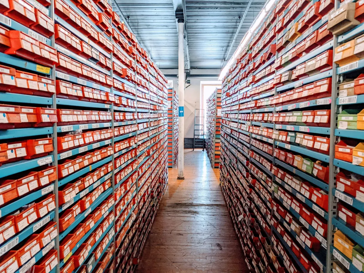 Corredor de um armazém com prateleiras cheias de caixas organizadas para entender O Que É FIFO Estoque e como evitar perdas de mercadorias por vencimento.