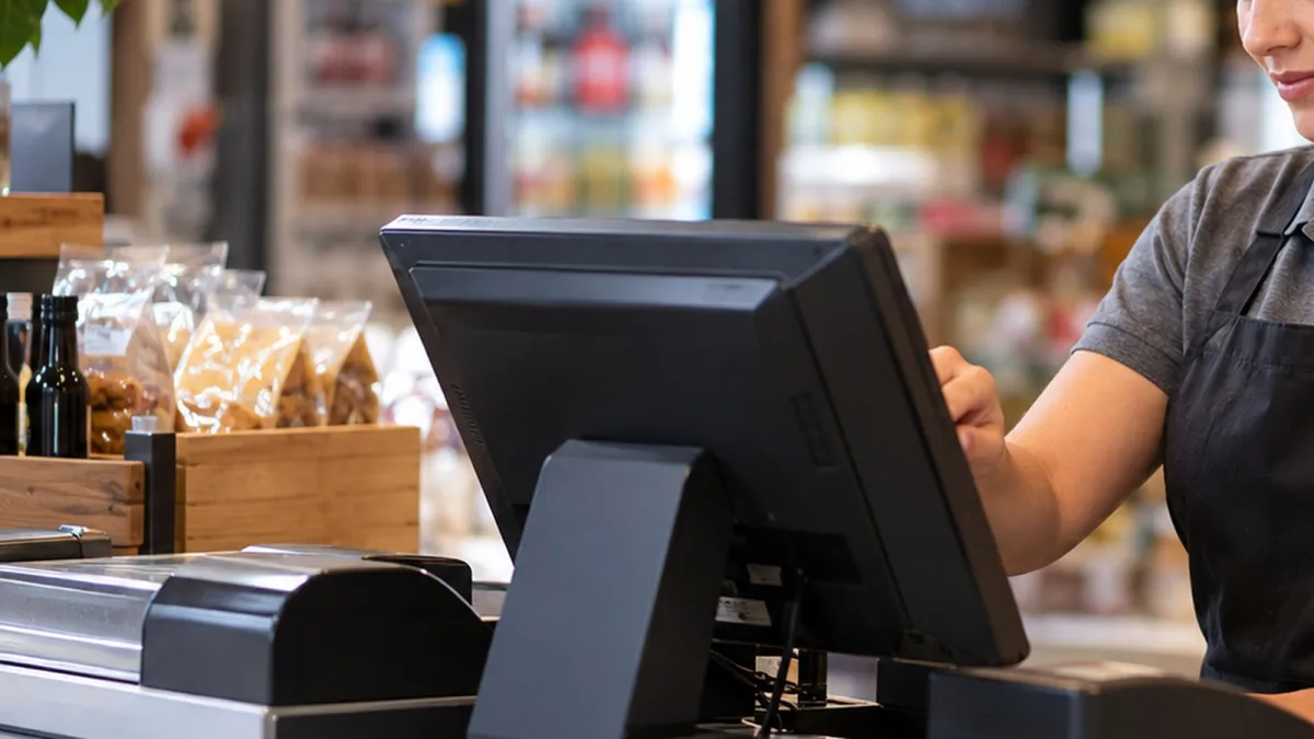 Monitor de PDV, leitor de código de barras e impressora térmica organizados sobre um balcão comercial.