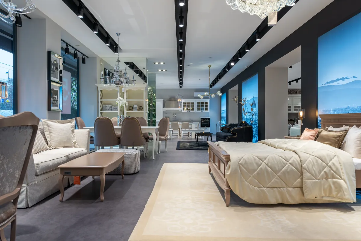 Sala de estar moderna com sofá em L bege, poltrona e mesa de centro quadrada com vidro e acabamento em madeira, em ambiente decorado com iluminação de trilho no teto.