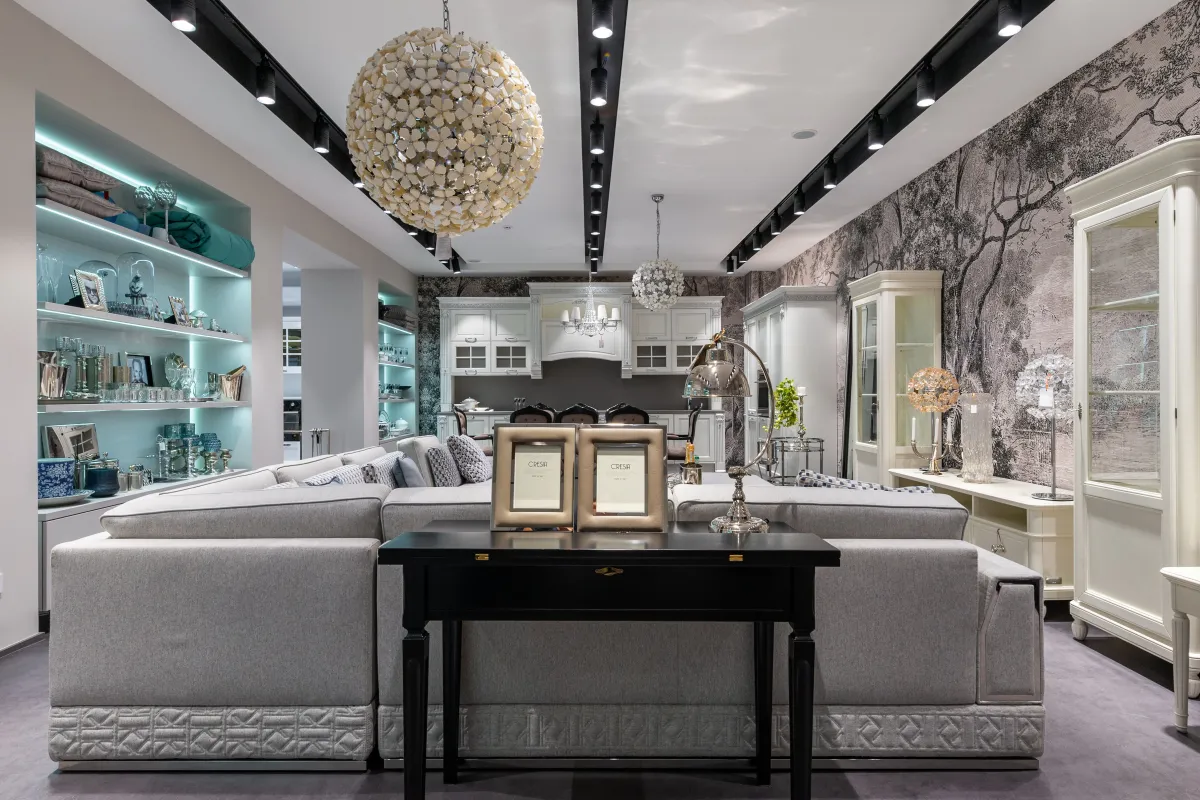 Sala de estar elegante em ambiente decorado com sofá cinza, mesa de madeira preta, iluminação embutida e luminária de teto em estilo candelabro, com detalhes em prateleiras e espel