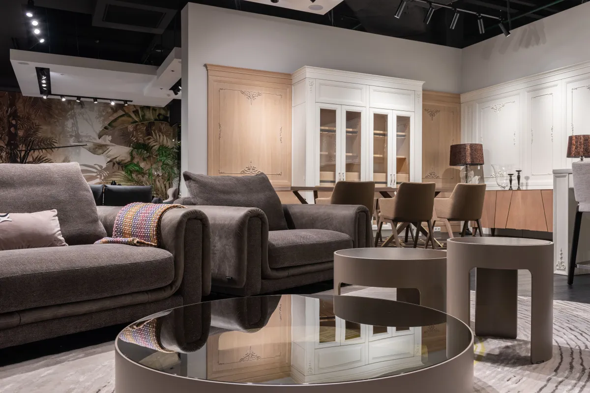 Sala de estar decorada em showroom de móveis, com sofás em tecido cinza, poltronas, mesa de centro redonda e armário planejado com portas de vidro e iluminação ambiente