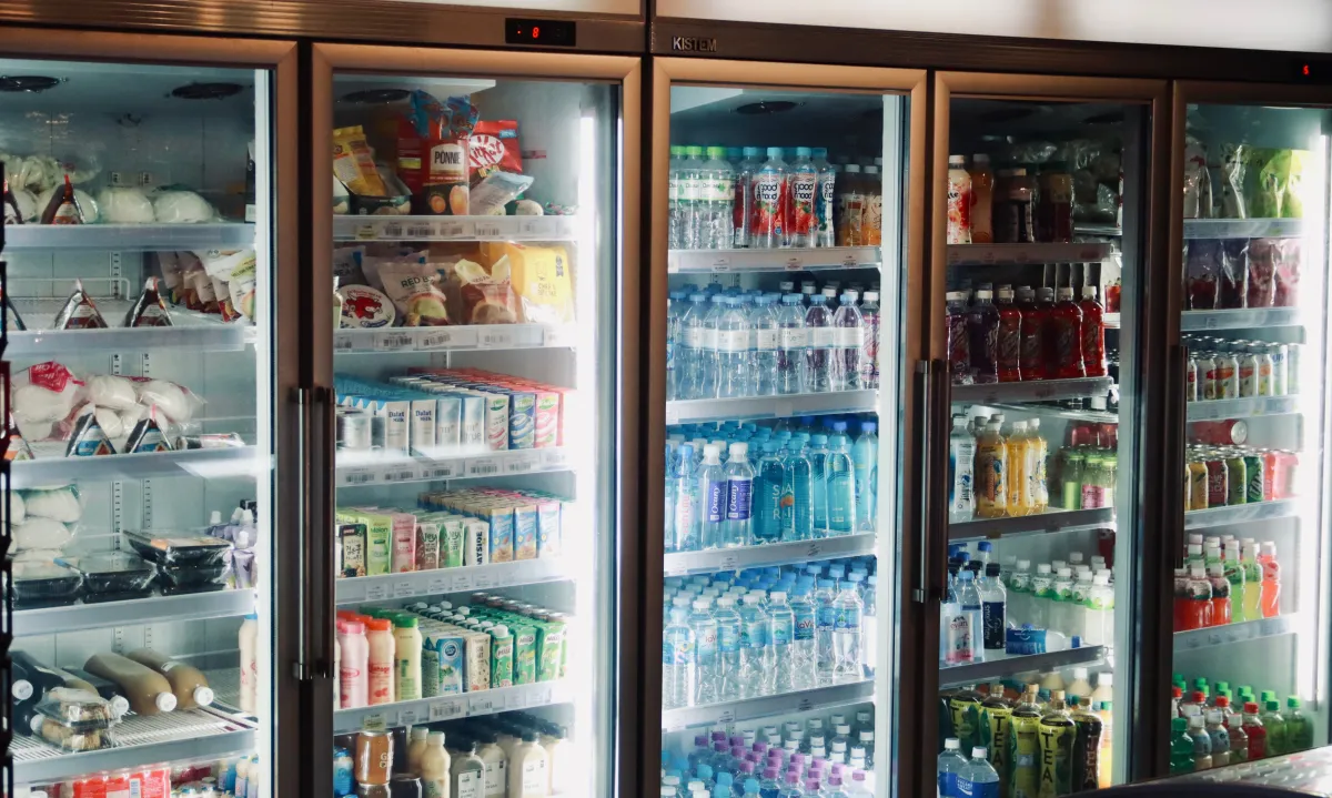 Refrigerador comercial com bebidas e alimentos dispostos em prateleiras.