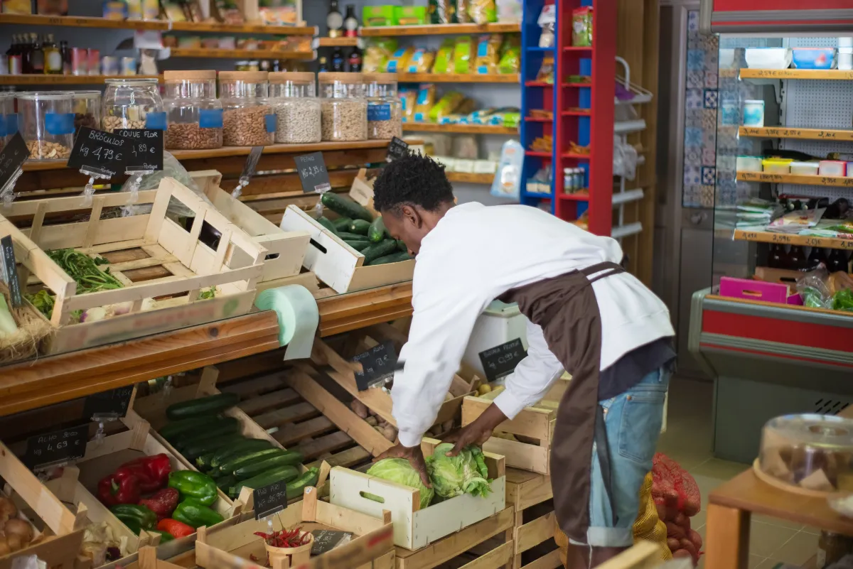 Funcionário de mercado organizando verduras e alimentos na área de exposição.