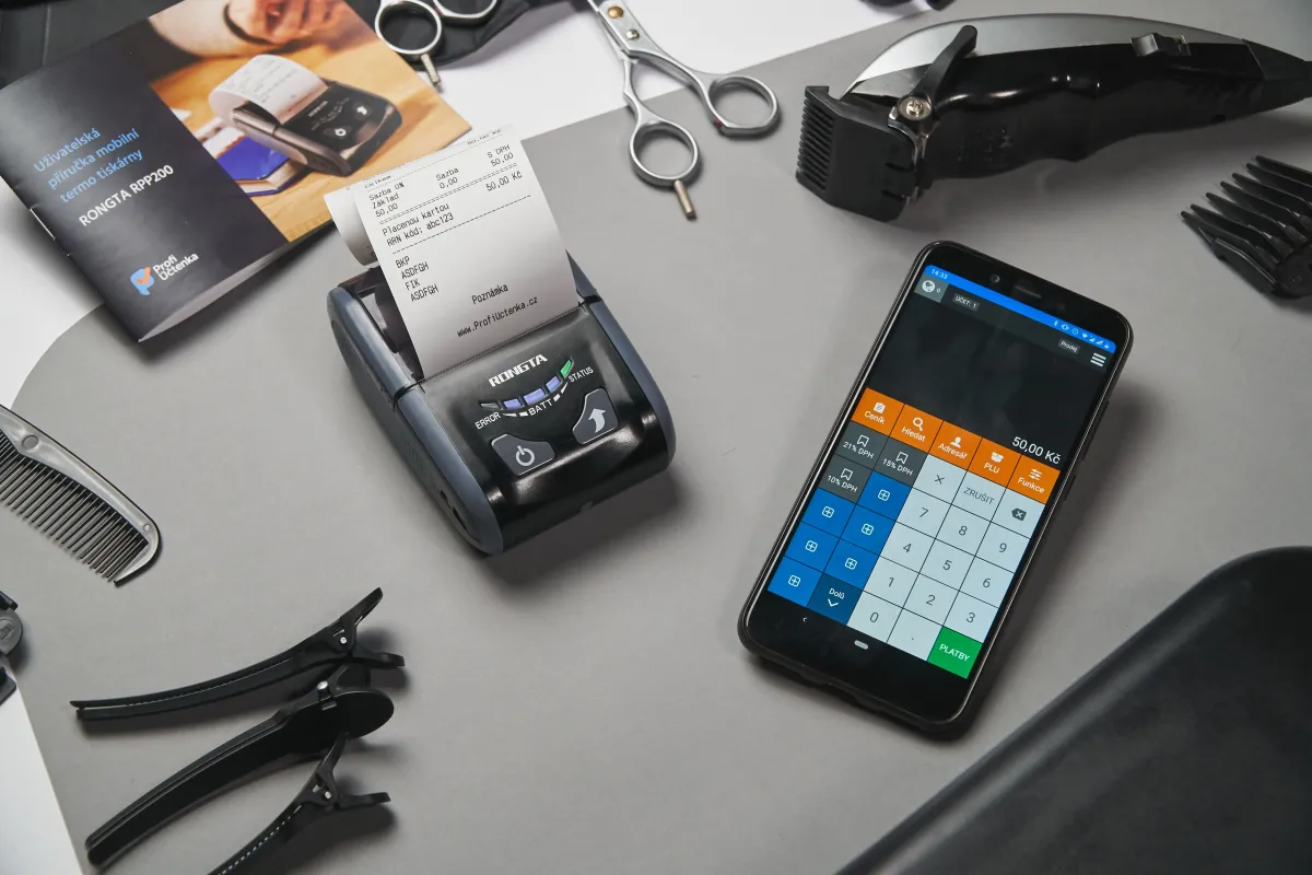 Atendimento em loja: pessoa em pé com avental laranja segura um tablet enquanto outra pessoa usa o celular para realizar pagamento ou confirmação. Ao lado há planta em vaso e jarra