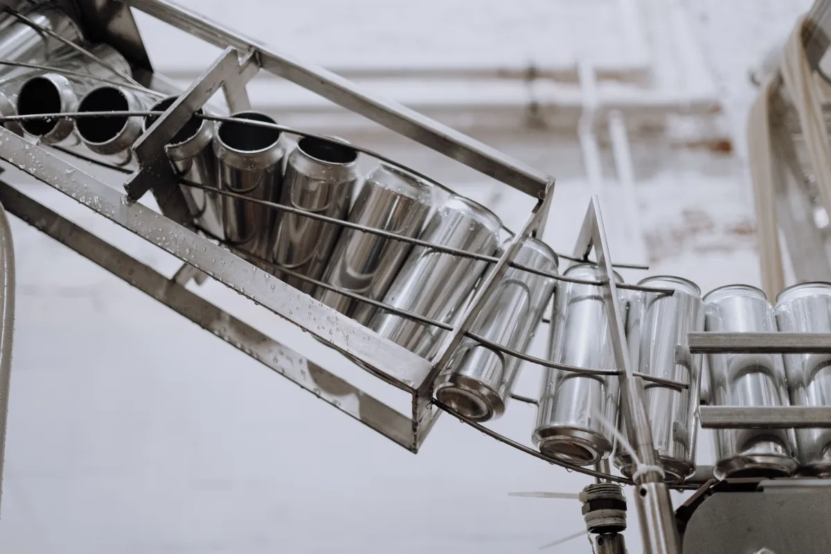 Close-up de instrumentos de aço inox em uma linha de envase, com copos metálicos e suportes montados em estrutura industrial.