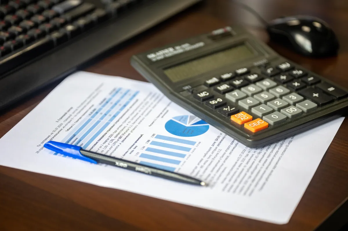 Planilha e relatório financeiro com gráficos e tabelas impressos sobre uma mesa, ao lado de uma calculadora e um lápis, sugerindo análise de custos e indicadores.