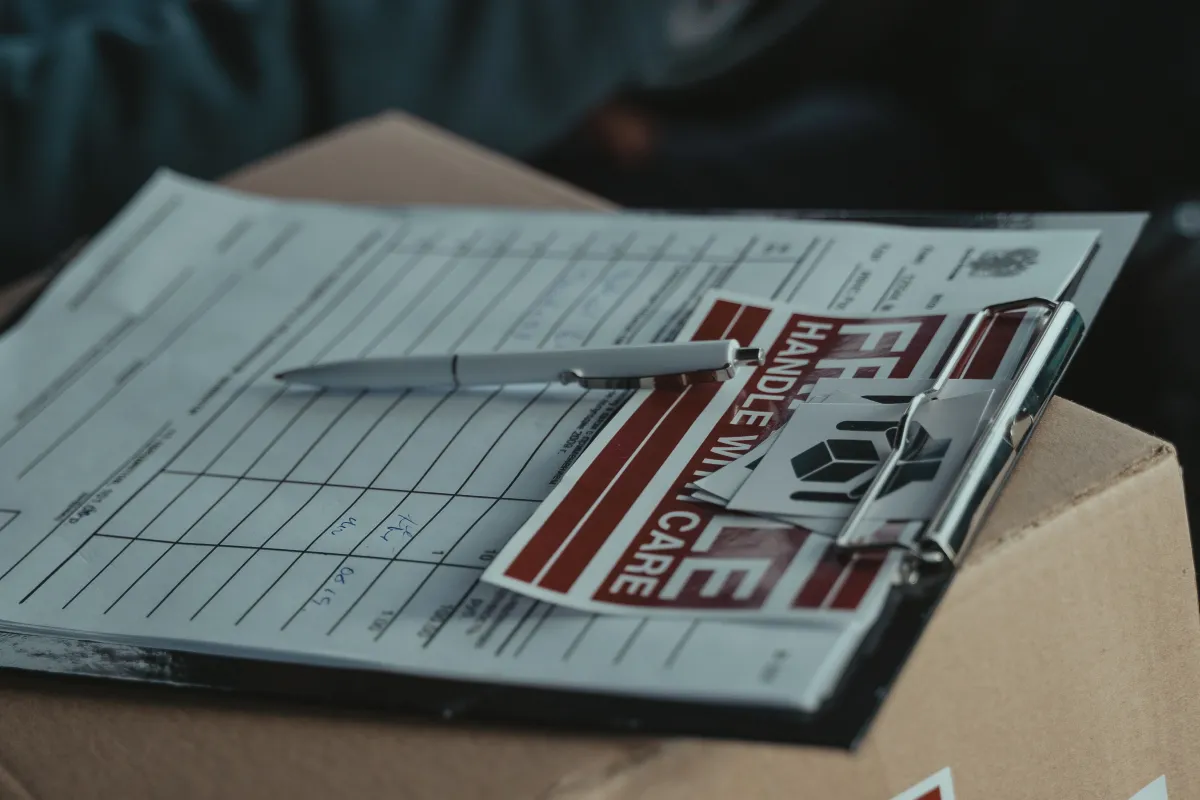 Prancheta com documentos sobre uma caixa de papelão, representando a verificação de informações de uma entrega.