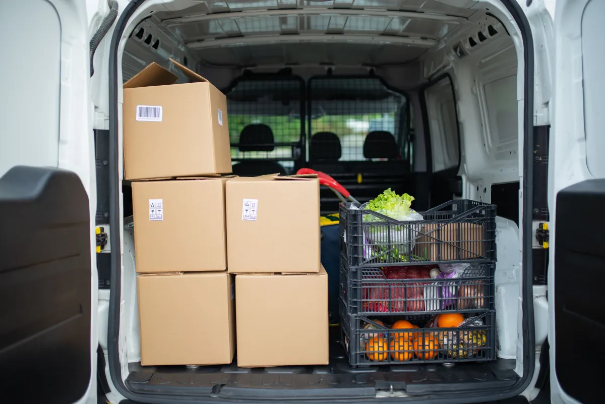 Caixas e produtos alimentícios organizados no interior de um veículo de entregas.