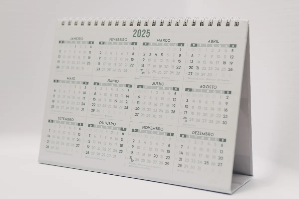 Calendário de mesa 2025 com páginas mensais visíveis, mostrando meses como janeiro, fevereiro, março, abril, maio, junho e outros, com datas em destaque e layout organizado.