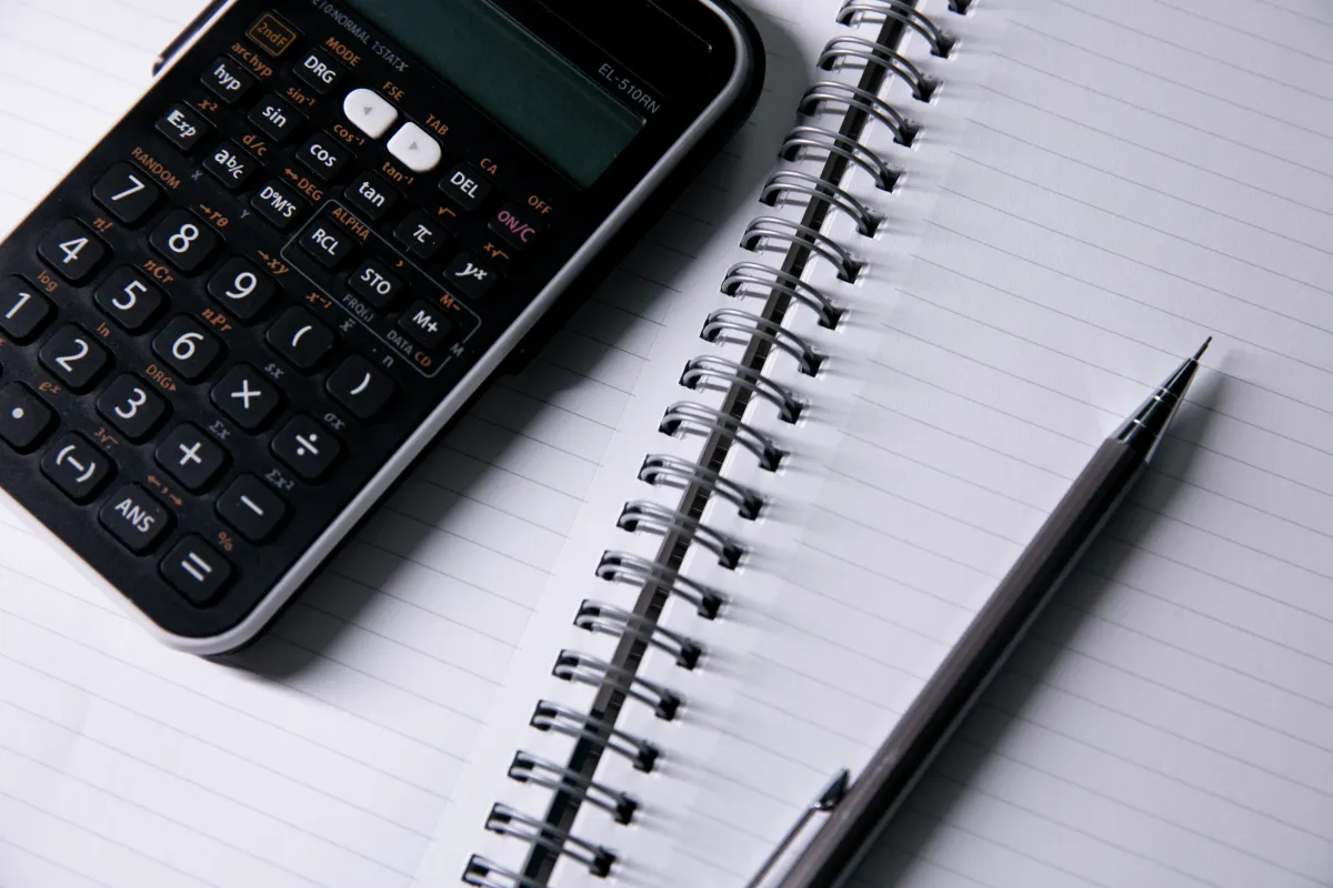Caderno aberto com calculadora e caneta para controle manual de pagamentos.