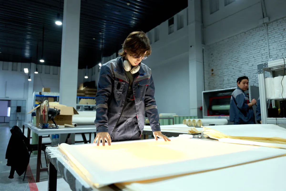 Trabalhador examinando chapas em uma fábrica, representando a verificação de materiais antes da produção.