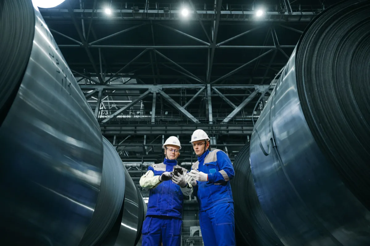 Profissionais inspecionando bobinas de aço em uma instalação industrial.