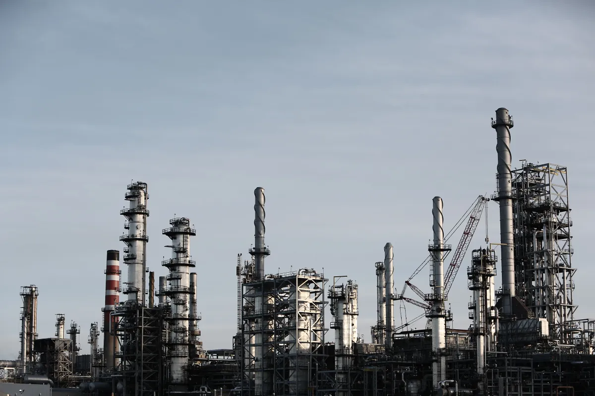 Parque industrial com várias chaminés e estruturas metálicas, mostrando uma refinaria ou planta de processamento ao ar livre sob céu nublado.