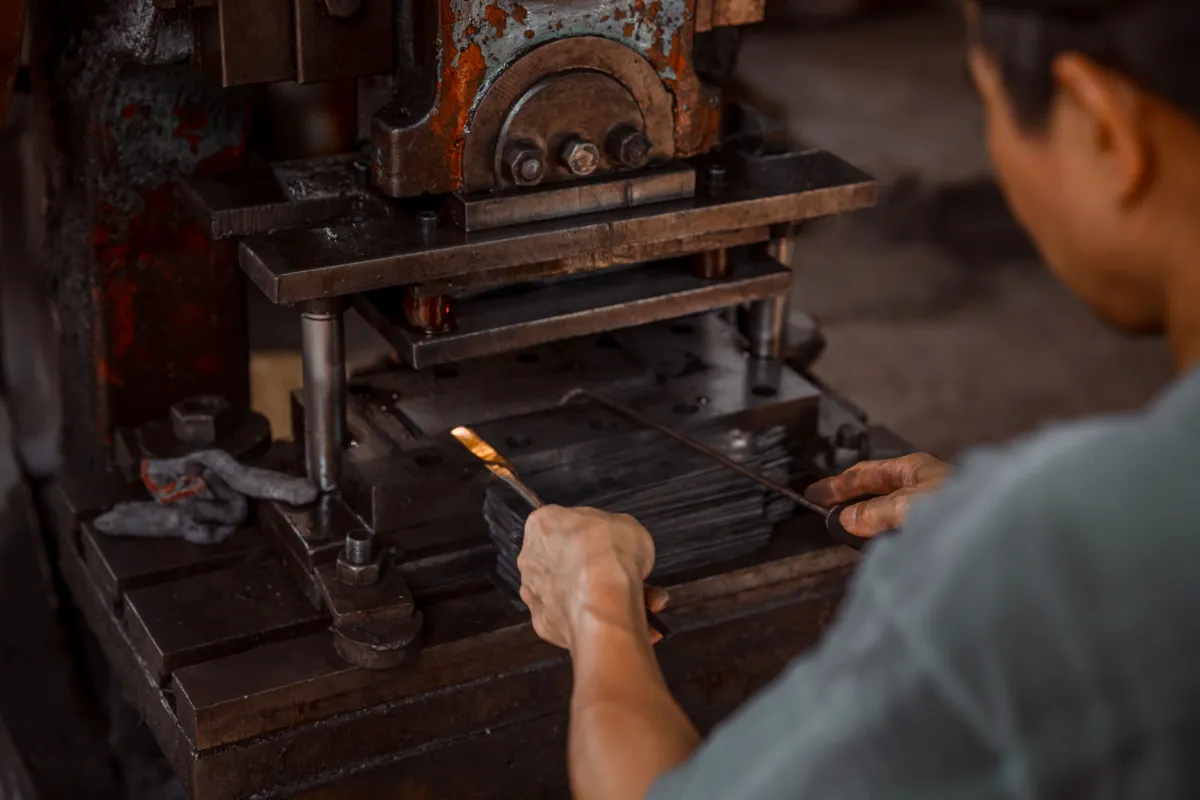 Operador utilizando uma prensa industrial durante o processo de fabricação de peças metálicas.