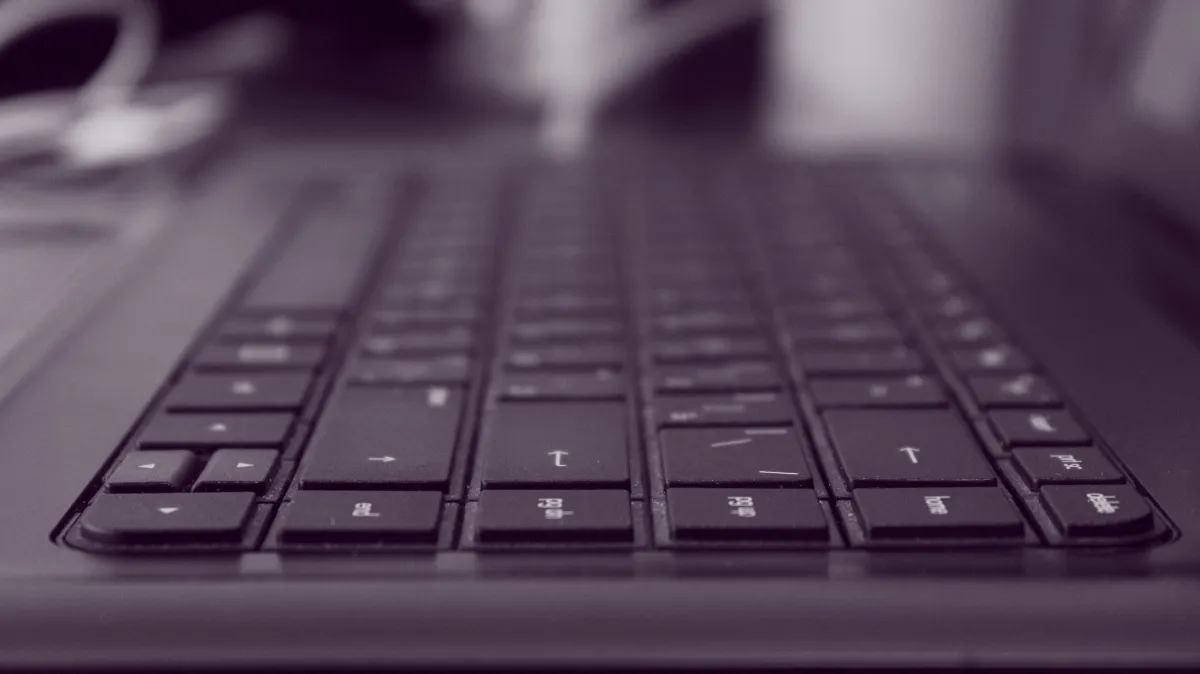 Vista em close de um teclado de computador, com teclas desfocadas ao fundo e foco nas teclas principais, em tons escuros e iluminação suave.