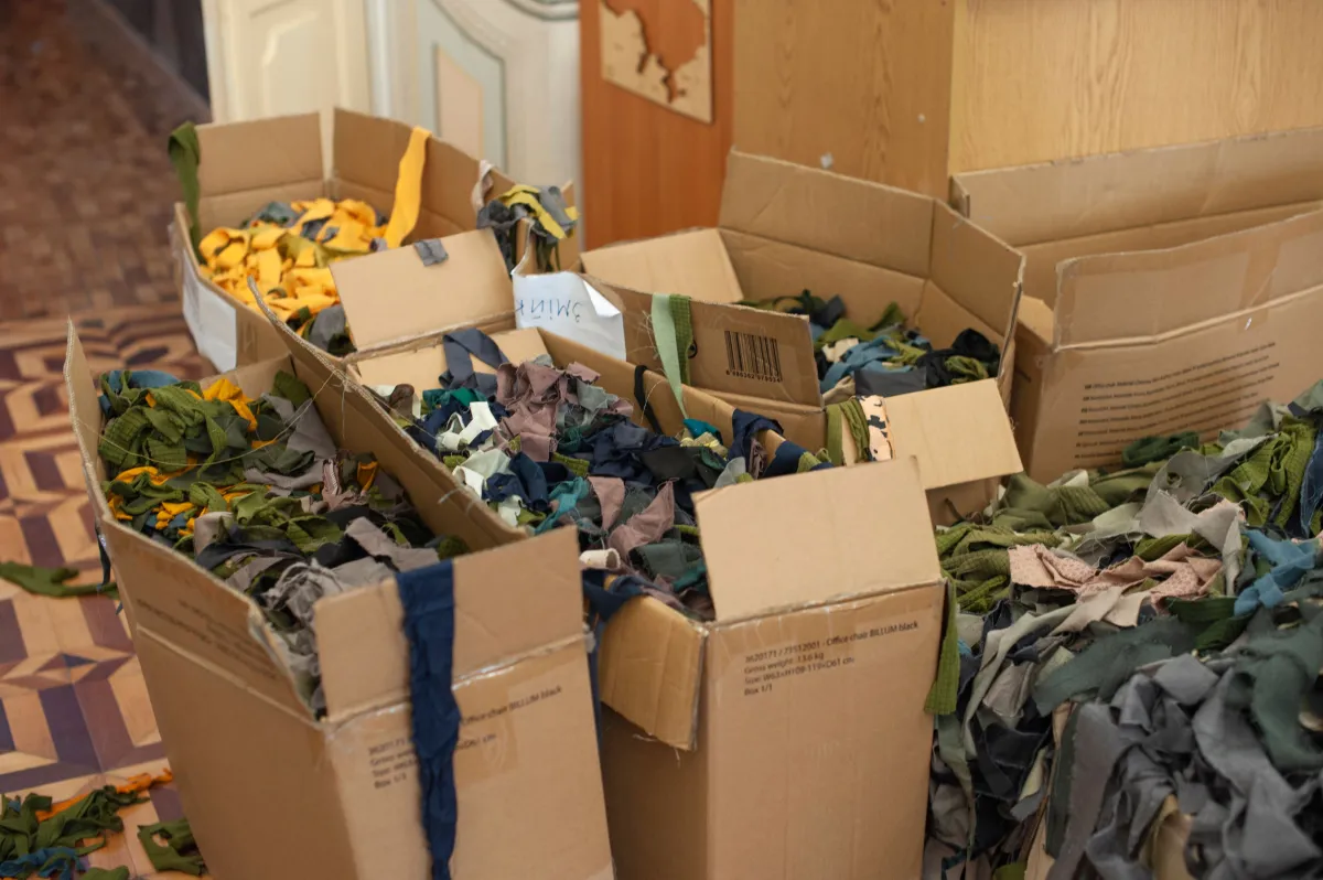 Caixas de papelão abertas com roupas e tecidos dobrados e amontoados, em um ambiente interno, prontas para triagem ou doação