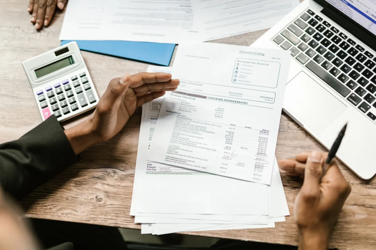 Conferência de documentos financeiros com calculadora e notebook para acompanhar os registros da empresa.