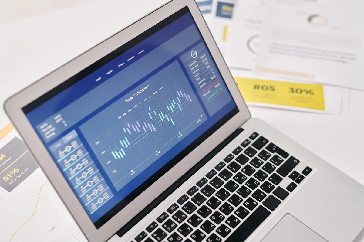 Sistema ERP em notebook com interface de gestão e gráficos no monitor, com teclado e documentos de apoio ao fundo em ambiente corporativo