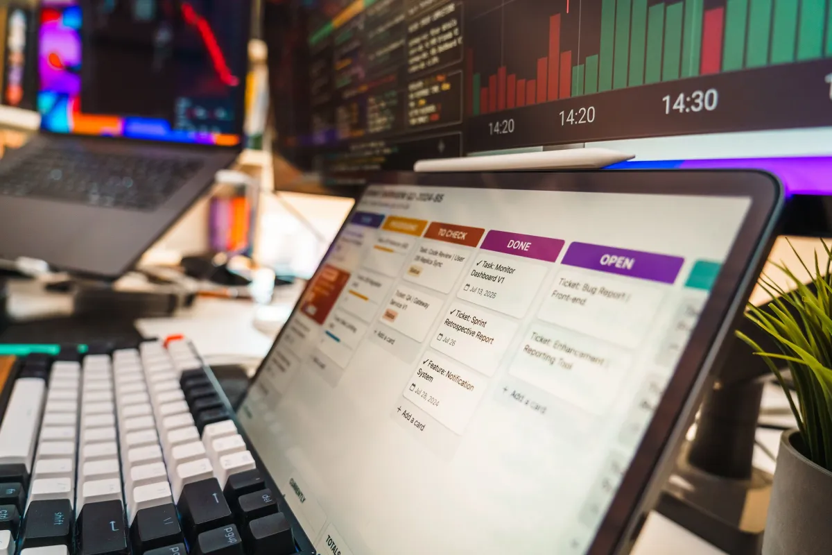 Sistema ERP em monitor com interface de tarefas e status Open, Done e outras listas, em ambiente de trabalho com teclados e gráficos ao fundo