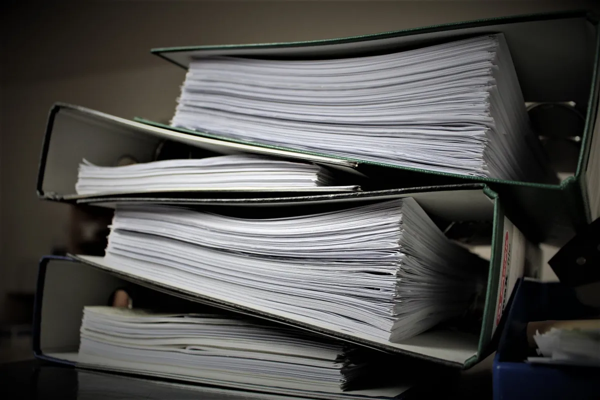 Pastas de arquivo empilhadas com grande quantidade de documentos em papel, representando o acúmulo de tarefas manuais.