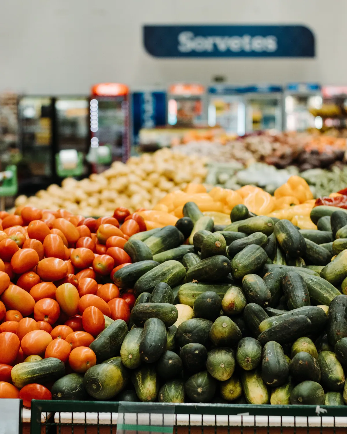Pepinos e tomates vibrantes em exibição na seção de produtos de um supermercado brasileiro.