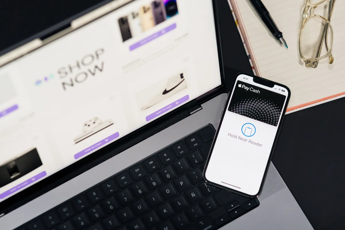 Notebook e smartphone exibindo ambientes de compras online, com foco na utilização da tecnologia.